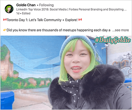 To jest zrzut ekranu wideo LinkedIn, w którym Goldie Chan dokumentuje swoje podróże. Tekst nad filmem brzmi: „Toronto - dzień 1: Porozmawiajmy o społeczności + odkrywaj! Czy wiesz, że każdego dnia odbywają się tysiące spotkań?.. Zobacz więcej". Wideo przedstawia Goldie przed muralem na ścianie z cegły. Mural przedstawia błękitne niebo i brązowe klify pokryte jasną zielenią. Goldie pojawia się od klatki piersiowej w górę. Jest Azjatką o zielonych włosach. Ma na sobie niebieską czapkę z dzianiny i czarną kurtkę z futrzanym kołnierzem. W prawym górnym rogu filmu #DailyGoldie pojawia się brzoskwiniowym tekstem z zieloną obwódką.