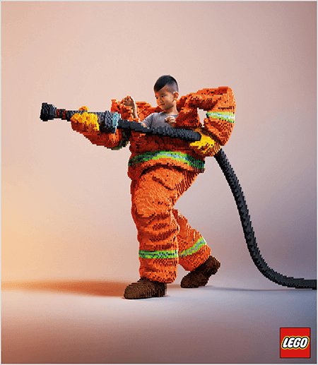 To jest zdjęcie z reklamy LEGO, która przedstawia młodego Azjatę w mundurze strażaka wykonanym z LEGO. Mundur jest pomarańczowy z neonowo-zielonym paskiem wokół mankietów płaszcza i spodni. Strażak stoi z jedną stopą do tyłu i trzyma wąż strażacki, również wykonany z klocków Lego. Głowa chłopca wyłania się z wierzchu munduru, który jest znacznie większy niż on i zatrzymuje się na ramionach. Zdjęcie zostało zrobione na zwykłym neutralnym tle. Logo LEGO pojawia się w czerwonym polu w prawym dolnym rogu. Talia Wolf twierdzi, że LEGO to świetny przykład marki, która wykorzystuje emocje w reklamie.